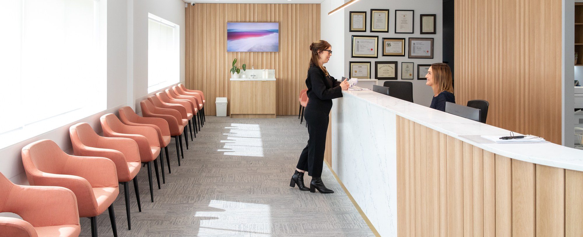 A patient checking in at the Eastwood Eye Surgery reception desk beside the sunlit waiting area
