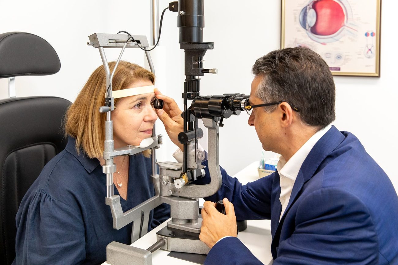 Ophthalmologist examining a patient's eye at a slit lamp using a handheld lens