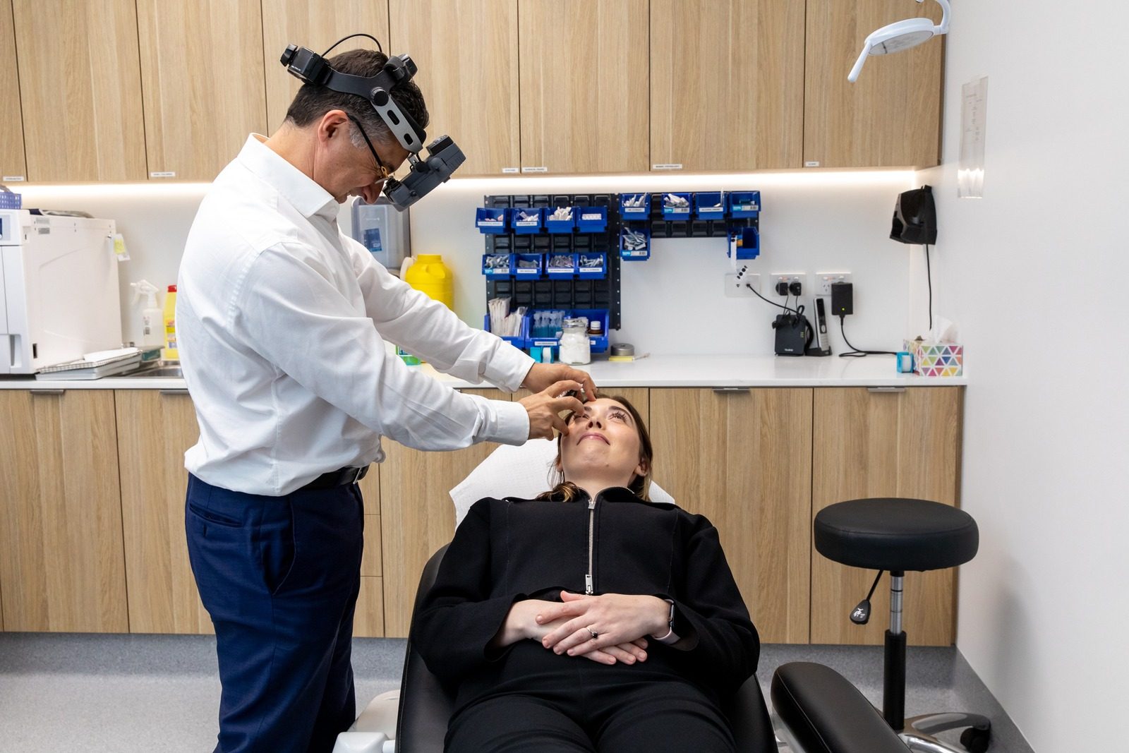 Ophthalmologist wearing a head-mounted indirect ophthalmoscope examining the retina of a reclined patient at Eastwood Eye Surgery