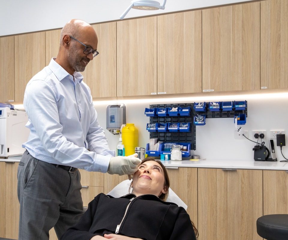 Ophthalmologist wearing a surgical glove examining a reclined patient's eye in the procedure room at Eastwood Eye Surgery